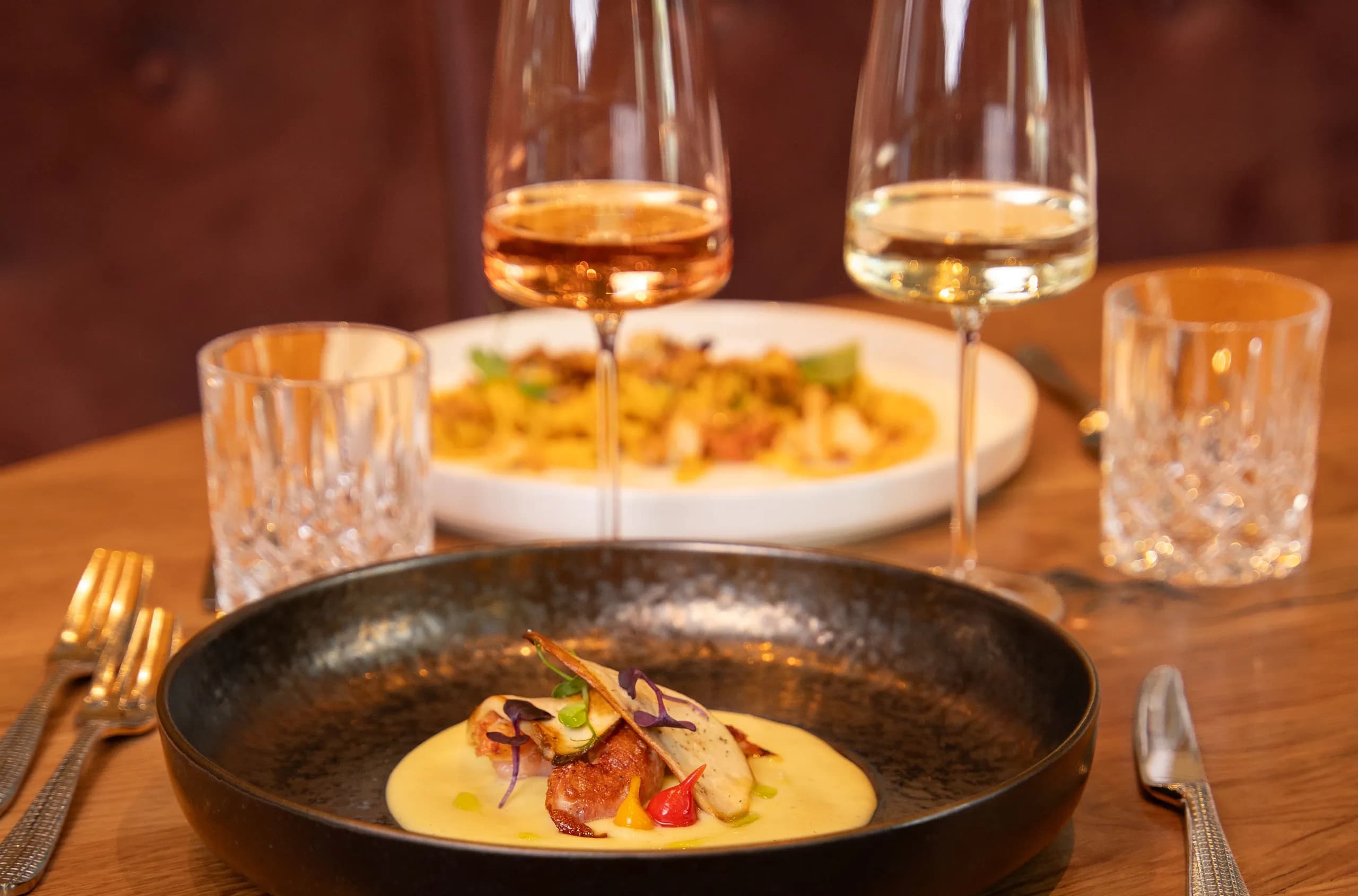 Ein gedeckter Tisch mit zwei angerichteten Tellern und zwei Gläsern Wein